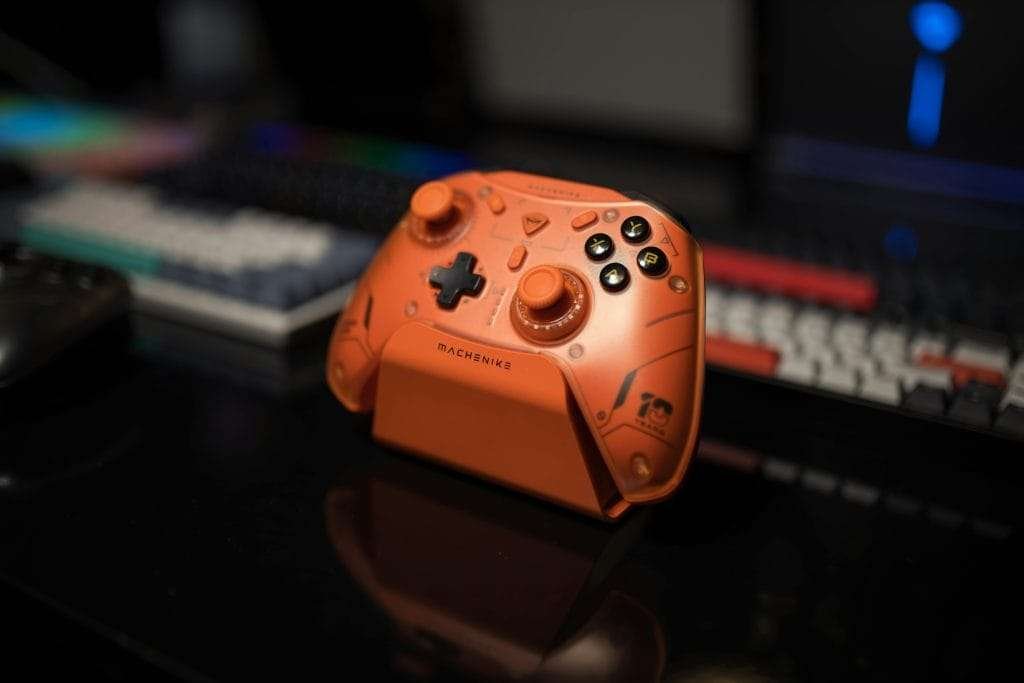 桌上擺放橘色遊戲手把,背景鍵盤微光閃爍